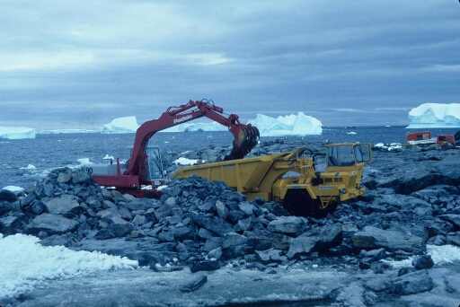 Le chantier de construction de la piste du Lion, les engins de travaux publics en action. En arrière-plan, des icebergs dans une mer libre.