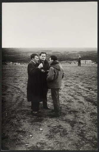 Trois hommes discutent sur un terrain vague d'une base