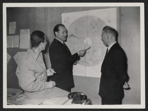 Trois hommes devant une carte dont l'un fait une démonstration.