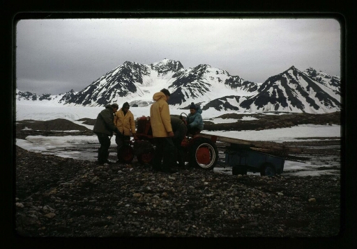 Cinq hommes autour d'un tracteur rouge et une remorque bleue dans le paysage du Spitzberg - mission CNRS 1964