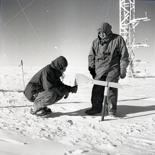 Au pied de la tour météo, deux hommes s'intéressent à la girouette plantée sur la glace.