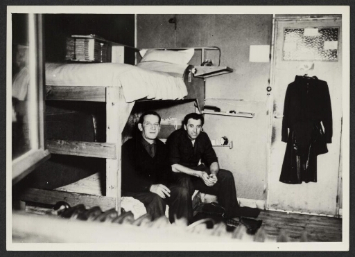 Deux hommes assis sur un lit. Intérieur d'une chambre