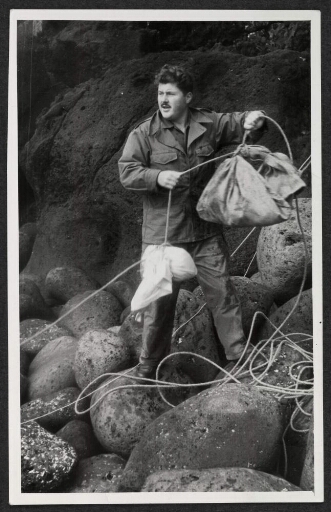 Un homme debout sur des rochers tient des sacs de lin accroché à des cordes