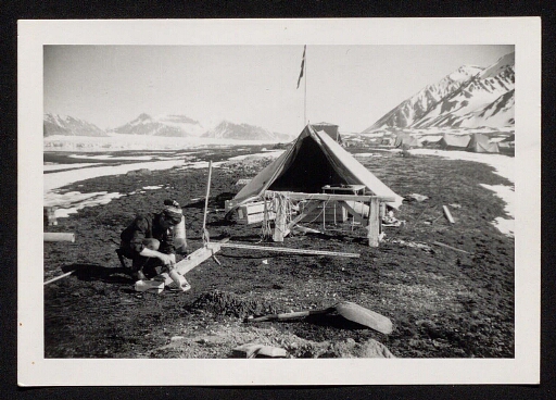 Un homme travaille au plein air devant une tente, base Corbel - mission CNRS 1964,