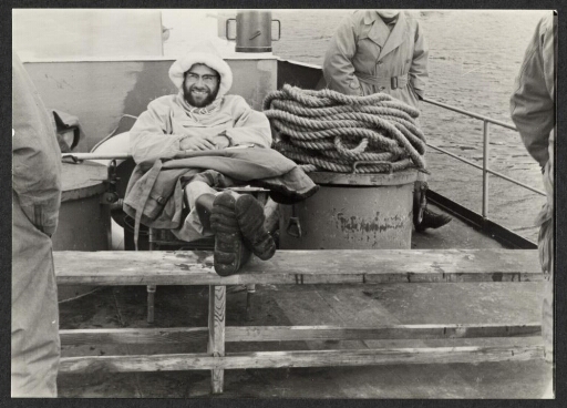 Un homme souriant assis les pieds croisés sur un bateau