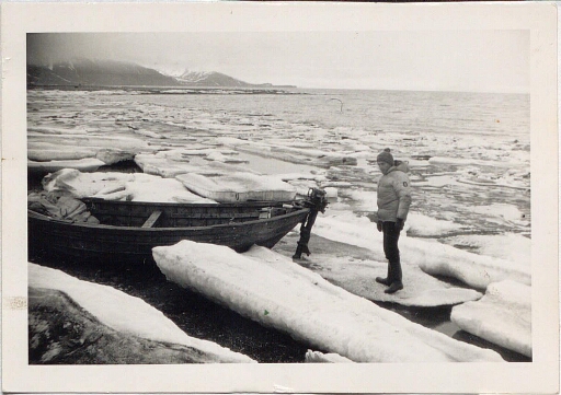 Un homme debout sur un morceau de glace près d'une barque en bois