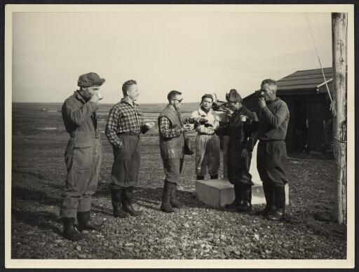 Un groupe d'hommes prennent une collation devant une cabane et une stèle