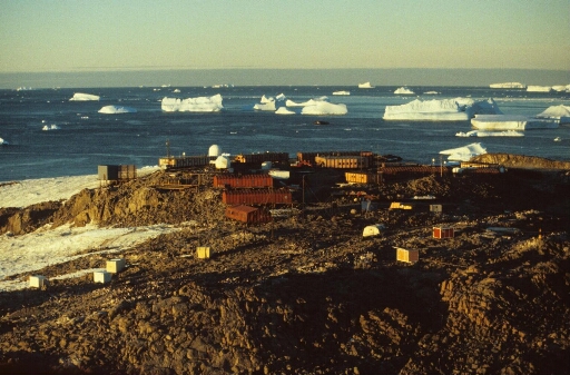 Survol à basse altitude, vers le nord-est, du centre de la base. Mer libre à perte de vue. Nombreux icebergs. Lumière du couchant.
