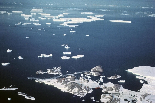 Survol, vers le nord-est, de l'archipel, le front de l'Astrolabe et, au sud des grands icebergs, le rocher du Débarquement. Le Magga Dan amarré aux Pétrels.