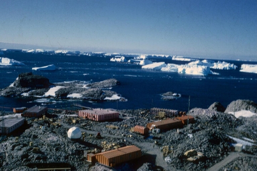 Survol, vers le nord-est, du centre de la base et de l'île du Lion. Mer libre et icebergs à perte de vue. Très beau temps calme.