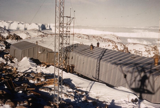 Les deux premiers bâtiments  de la base Dumont d'Urville construits pour l'AGI. En arrière plan, l'Astrolabe et des icebergs.