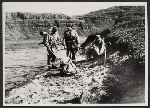 Quatre hommes s'arrêtent près d'un cours d'eau. Un sac au milieu et sur le sol