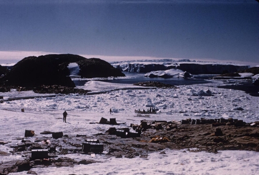 Vue sur la zone de débarquement au sud de l'île des Pétrels. Une chaloupe et ses occupants manoeuvrant dans le pack. Le glacier de l'Astrolabe.