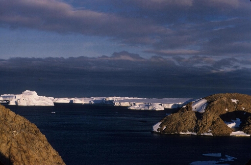 Photo prise au couchant depuis l'île des Pétrels en direction du glacier de l'Astrolabe et ses icebergs. A droite les îles Buffon et Claude Bernard.