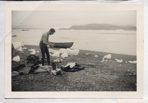 Une personne avec un pantalon de combinaison  de plongée bouteille près de matériels et de vêtements, à coté de morceaux de glace échoués sur le bord de mer