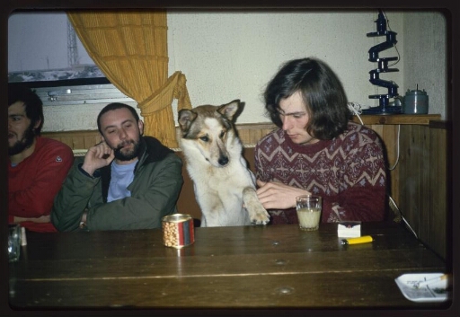 Trois hommes attablés prennent un verre, un chien est présent.