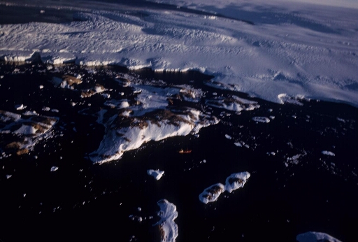 Vue aérienne vers le sud-est : l'archipel puis le glacier de l'Astrolabe. Le Magga Dan au mouillage sur la côte ouest de l'île des Pétrels. Mer libre.