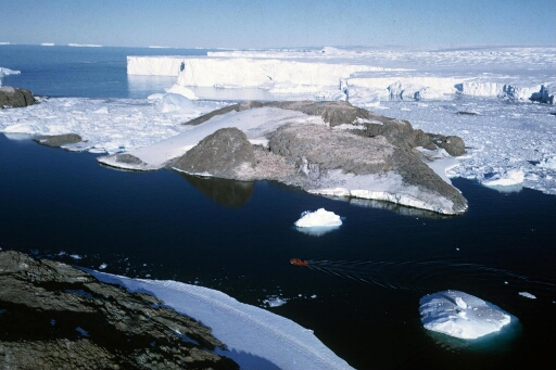 Vue depuis l'île des Pétrels de l'île Jean Rostand. En arrière-plan le glacier de l'Astrolabe. Une embarcation navigue en eau libre.