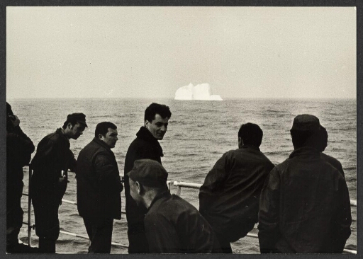 Des hommes sur le pont d'un navire, à l'arrière plan un iceberg. Au large de l'île des Pingouins