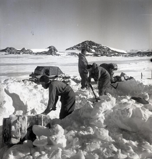 Quatre hommes s'emploient à la récupération de caisses enfouies sous la neige. Beau temps calme.