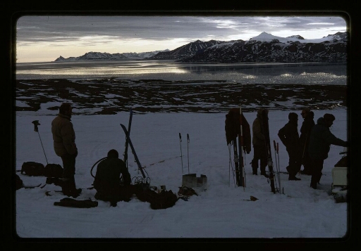 Une partie de l'équipe de Jean Corbel et des Russes près de divers matériels dont des skis, près d'un fjord - mission CNRS 1966