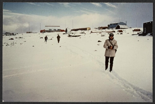 Trois hommes marchant dans la neige, en arrière plan la base Alfred Faure. 
