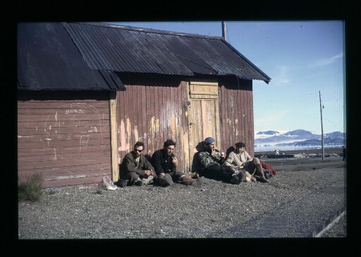 Quatres hommes assis  contre un baraquement dans le village de Ny-Ålesund - mission CNRS 1963