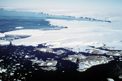 Vue aérienne à haute altitude vers le sud-est : l'archipel en direction du glacier de l'Astrolabe et le continent. Le nunatak du Bon Docteur. Mer libre, un peu de pack.