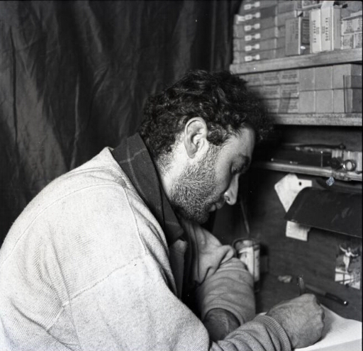 Le cinéaste-photographe Robert Pommier écrivant sous l'étagère de boites de films et pellicules photos.