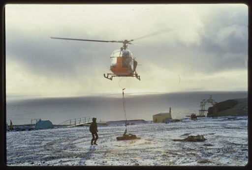 Chargement de matériel au sol par un hélicoptère de l'armée en vol stationnaire. Un homme au sol aidant à la manœuvre