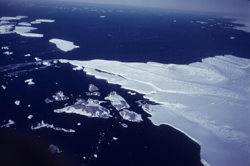 Survol à très haute altitude de l'archipel et du glacier de l'Astrolabe. Mer libre à perte de vue, quelques icebergs. Le Thala Dan entre les îles Pétrels et J. Rostand.