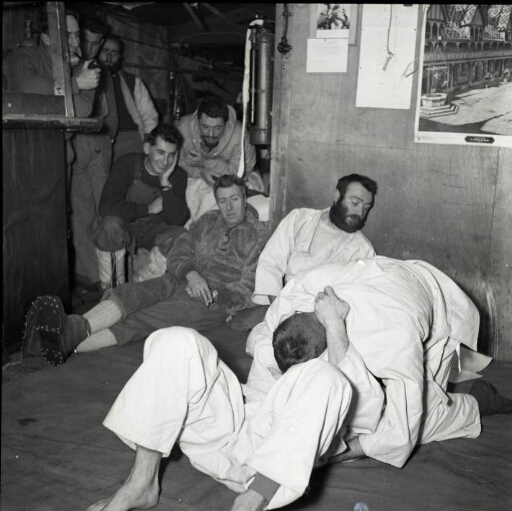 Sport et détente : deux hommes se livrent à un combat de judo sous l'œil de sept de leurs camarades.