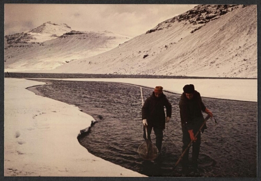 Deux hommes à la pêche à pied, un muni d'une épuisette et l'autre d'un générateur électrique, dans les déversoirs des lacs Studer durant l'hiver 1971.