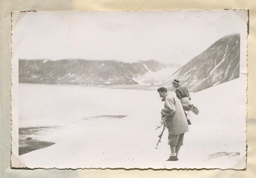 Deux hommes en tenue d'alpinisme qui regardent la glace entourés de montagne