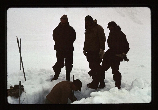 Quatre hommes, dont des Russes, debout regarde un homme dans un trou de neige- mission CNRS 1966