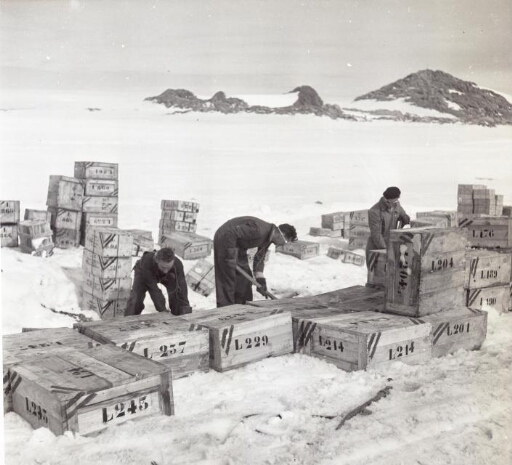 Trois hommes s'emploient à l'ouverture des caisses. A l'arrière plan, le Mont Chauve ?