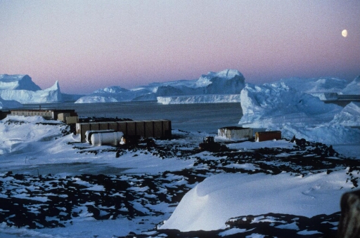 La base vie du chantier de la piste du Lion sous la neige au cours de l'hiver 1988. A l'arrière-plan les icebergs immobilisés par la banquise.