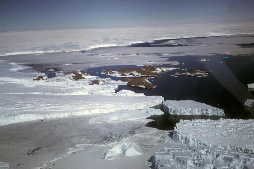 Survol du glacier de l'Astrolabe en direction du sud-ouest : l'île des Pétrels et les îles proches puis, vers le continent, l'île du Gouverneur et le cap Prudhomme.