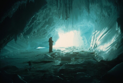 En fin d'hivernage, la banquise encore solide permet à cet hivernant d'explorer une grotte dans un iceberg. Lumière bleue caractéristique et stalactites.
