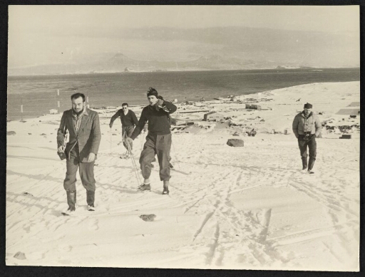 Cinq hommes qui marchent dont trois avec des batons de randonnées dans la neige. 