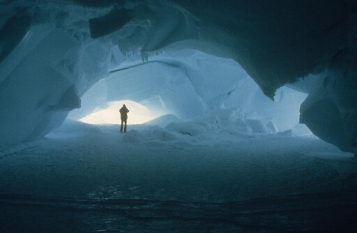 En fin d'hivernage, la banquise encore solide permet à cet hivernant d'explorer une grotte dans un iceberg. Lumière bleue caractéristique.